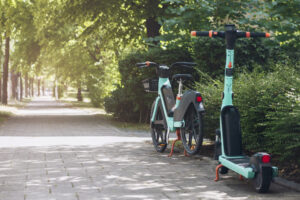 Electric bike and electric scooter parked beside a tree-lined path in New Jersey.